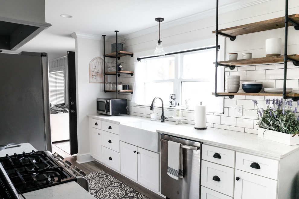 Small country galley kitchen in Charlotte with shaker cabinets, white cabinets, quartz benchtops, white splashback, no island, white benchtop, a farmhouse sink, subway tile splashback, stainless steel appliances and brown floor.