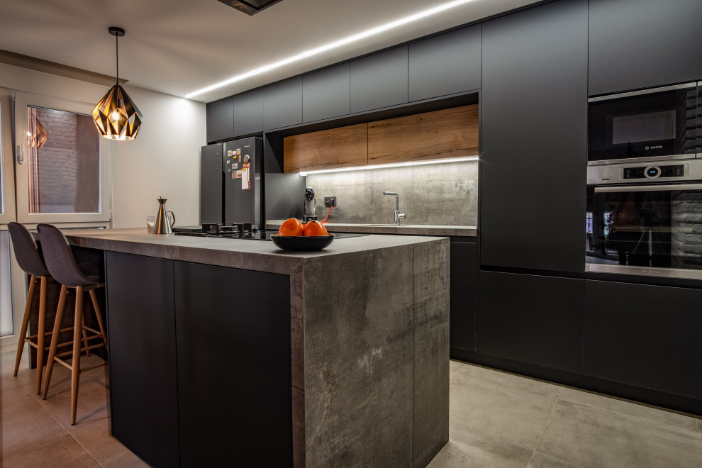 Inspiration for a mid-sized industrial eat-in kitchen in Other with flat-panel cabinets, black cabinets, tile benchtops, grey splashback, porcelain splashback, stainless steel appliances, medium hardwood floors, with island, brown floor and black benchtop.