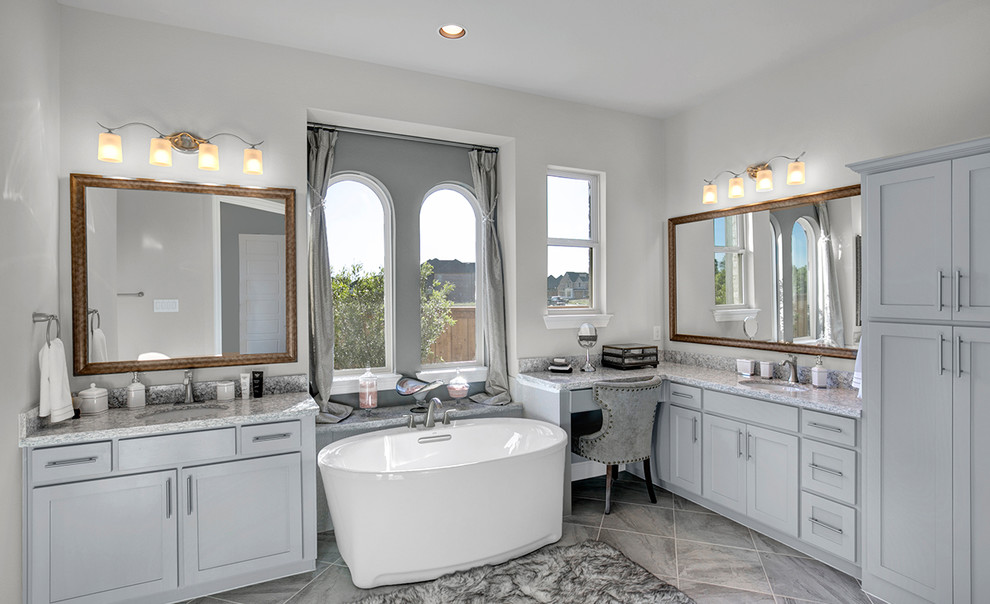Design ideas for a large contemporary master bathroom in Dallas with raised-panel cabinets, grey cabinets, gray tile, ceramic tile, granite benchtops, a freestanding tub, a double shower, grey walls, ceramic floors, an undermount sink, grey floor and a sliding shower screen.