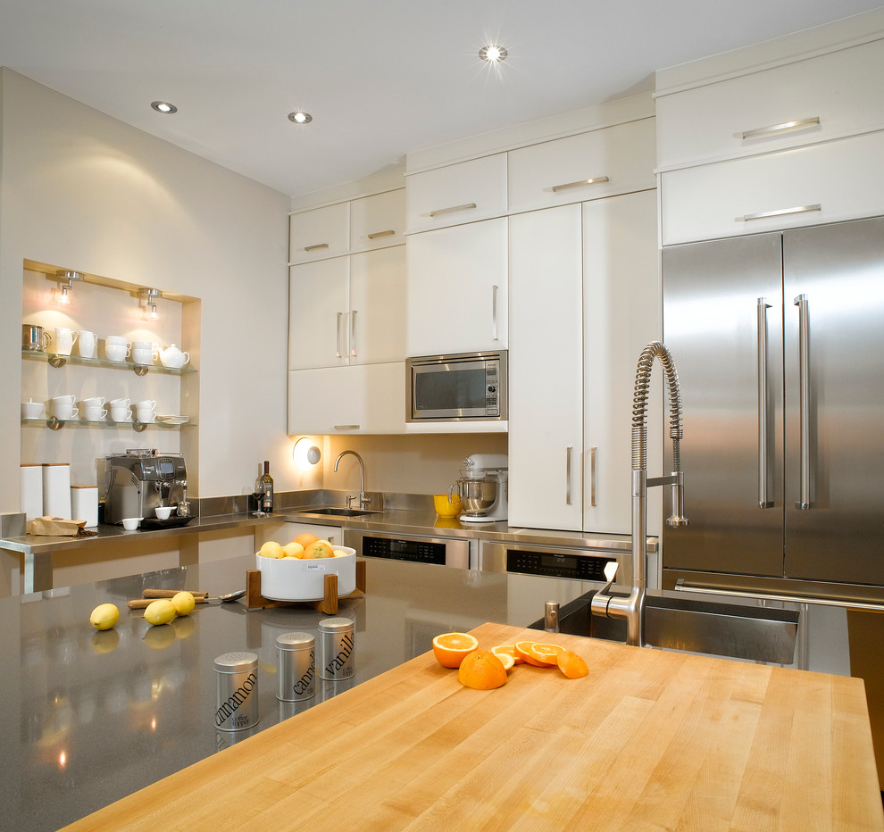 Inspiration for a large modern l-shaped eat-in kitchen in Montreal with stainless steel appliances, an undermount sink, flat-panel cabinets, white cabinets, quartz benchtops, metallic splashback, metal splashback, light hardwood floors and with island.