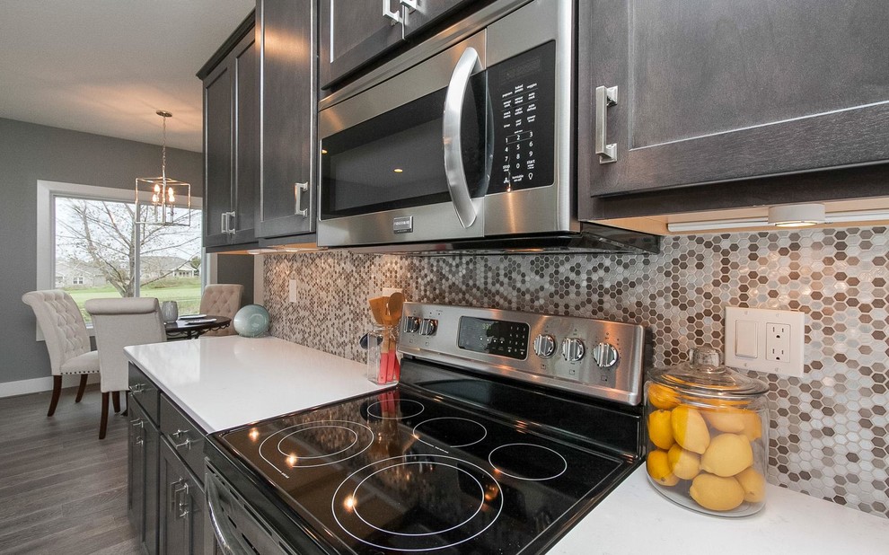 Large transitional single-wall light wood floor and beige floor eat-in kitchen photo in Cedar Rapids with a double-bowl sink, shaker cabinets, dark wood cabinets, solid surface countertops, multicolored backsplash, mosaic tile backsplash and an island