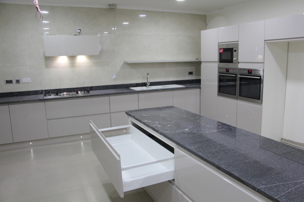 Design ideas for an expansive modern u-shaped separate kitchen in Other with a triple-bowl sink, flat-panel cabinets, grey cabinets, granite benchtops, beige splashback, porcelain splashback, stainless steel appliances, ceramic floors, with island, beige floor and black benchtop.