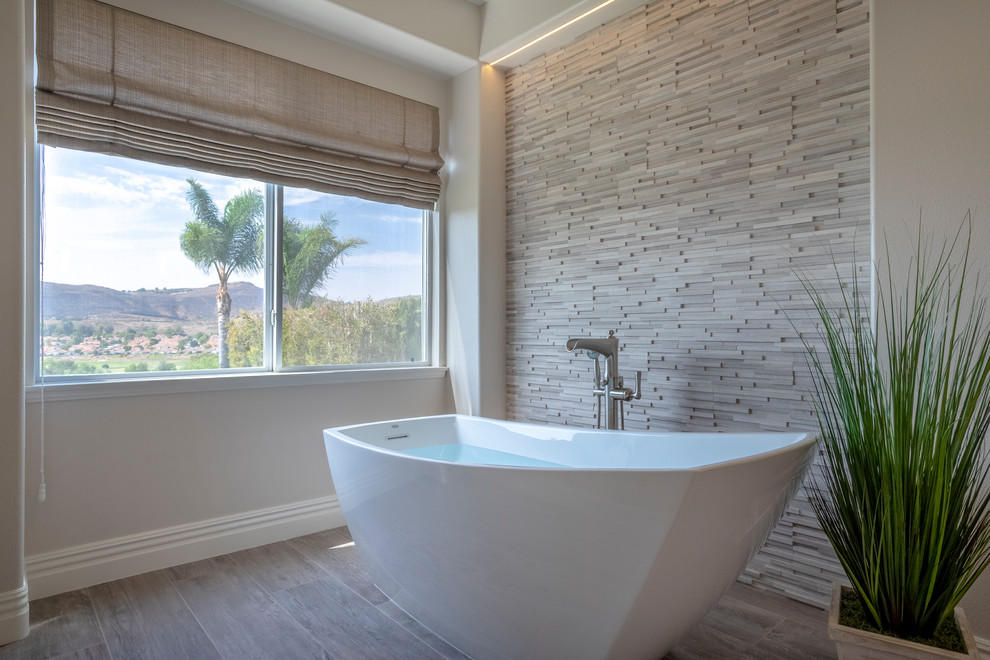 Large transitional master bathroom in Los Angeles with a freestanding tub, an open shower, gray tile, limestone, grey walls, porcelain floors, grey floor and an open shower.