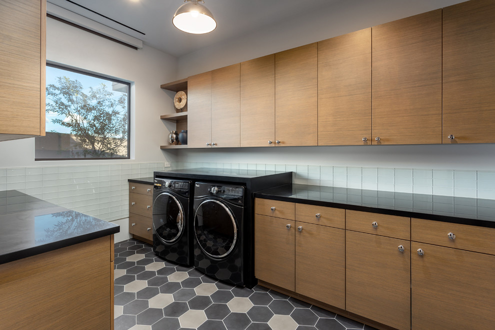 Photo of a contemporary dedicated laundry room in Phoenix with flat-panel cabinets, medium wood cabinets, white walls, a side-by-side washer and dryer, multi-coloured floor and black benchtop.