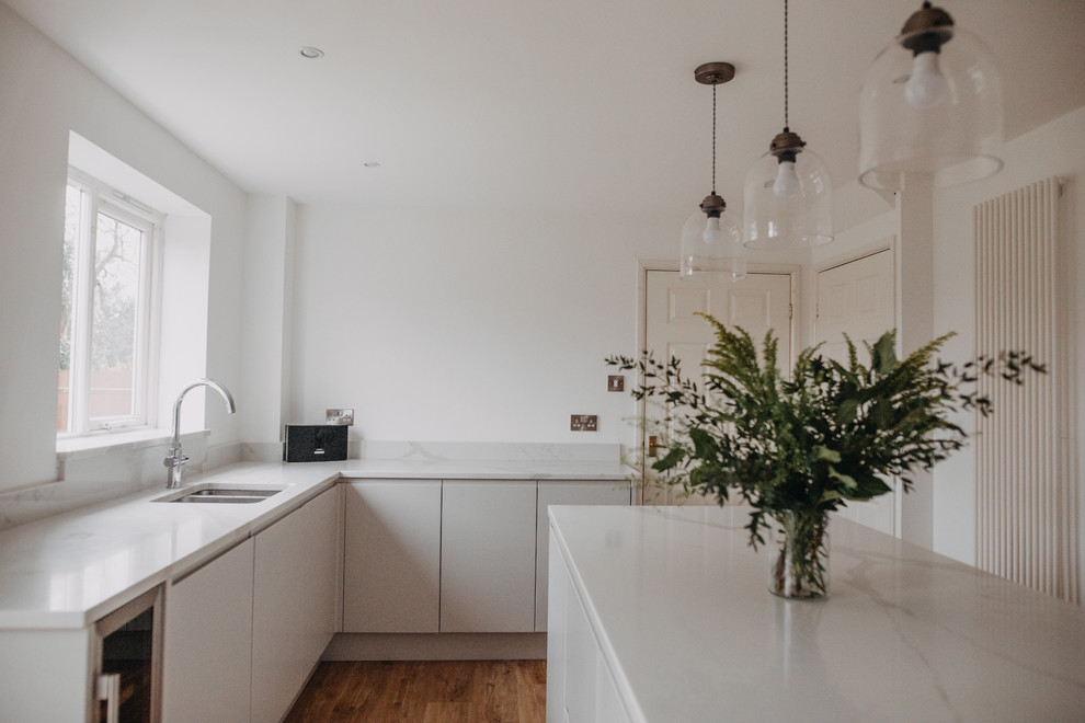 This is an example of a mid-sized modern eat-in kitchen in Other with an undermount sink, flat-panel cabinets, grey cabinets, quartzite benchtops, white splashback, black appliances, laminate floors, with island, brown floor and white benchtop.