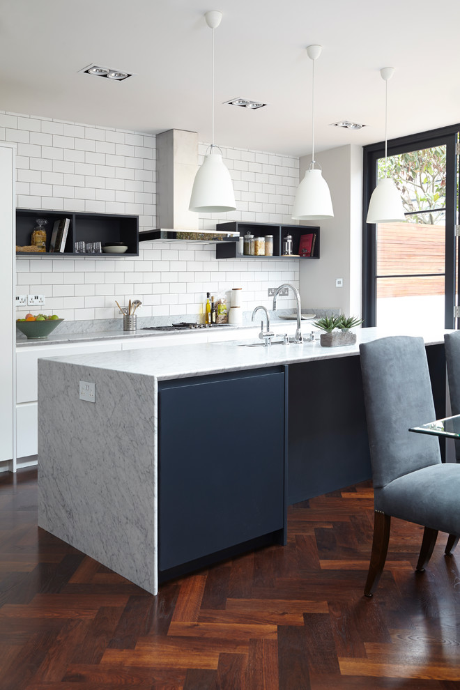 Inspiration for a transitional galley eat-in kitchen in London with flat-panel cabinets, white cabinets, white splashback, subway tile splashback, dark hardwood floors and with island.