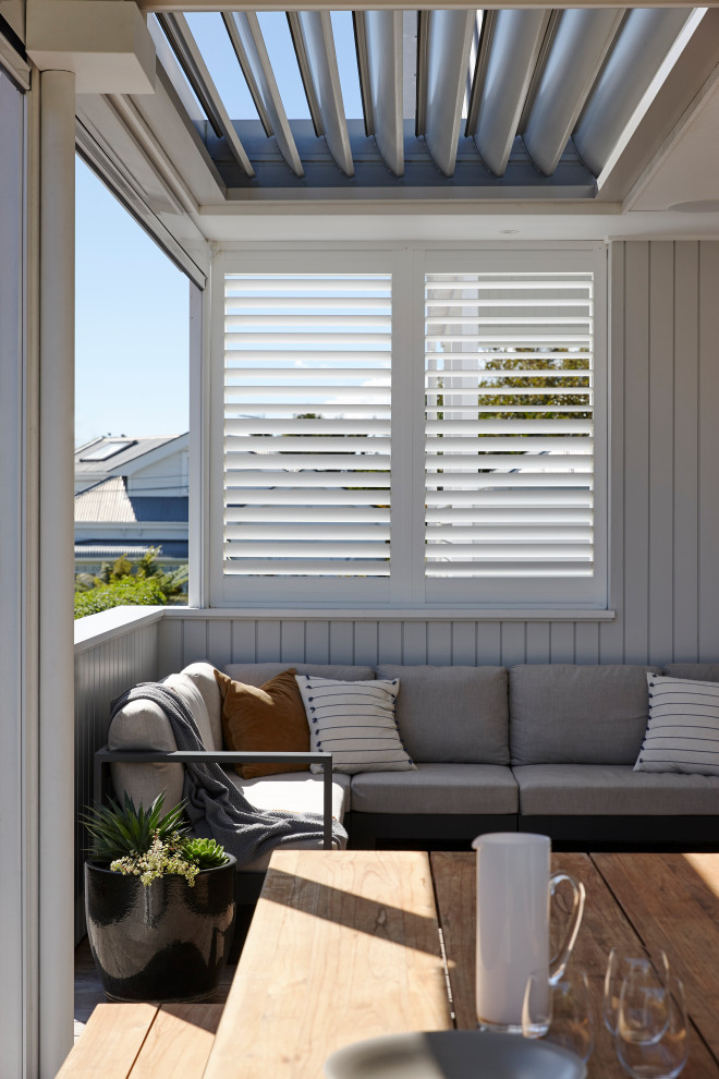 This is an example of a small contemporary side yard screened-in verandah in Auckland with decking, a roof extension and wood railing.
