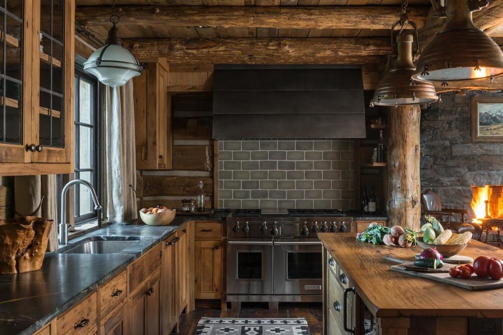 Photo of a country l-shaped open plan kitchen in Other with stainless steel appliances, with island, an undermount sink, medium wood cabinets, grey splashback, subway tile splashback and black benchtop.