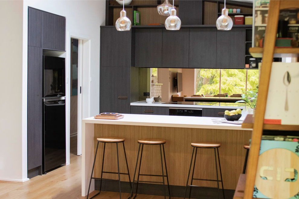 This is an example of a mid-sized midcentury u-shaped open plan kitchen in Adelaide with a double-bowl sink, flat-panel cabinets, black cabinets, quartz benchtops, brown splashback, glass sheet splashback, stainless steel appliances, medium hardwood floors, a peninsula, brown floor, white benchtop and exposed beam.