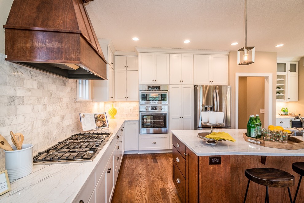 Large transitional l-shaped light wood floor and beige floor open concept kitchen photo in Minneapolis with a double-bowl sink, shaker cabinets, white cabinets, marble countertops, gray backsplash, marble backsplash, stainless steel appliances, an island and white countertops