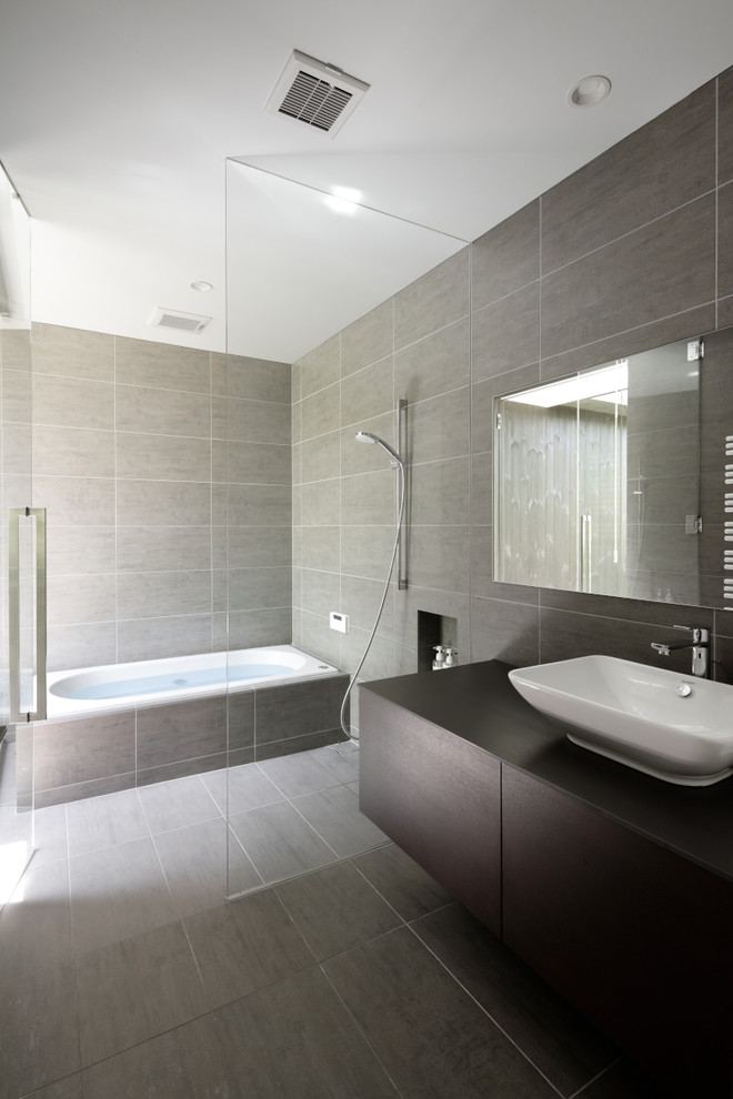 Modern bathroom in Other with brown cabinets, a drop-in tub, gray tile, porcelain tile, a vessel sink, engineered quartz benchtops, black benchtops, grey floor and flat-panel cabinets.