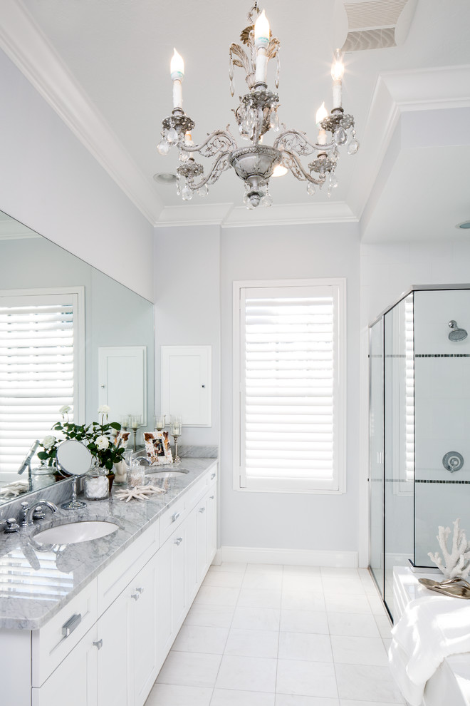 Photo of a mid-sized beach style master bathroom in Tampa with white cabinets, marble benchtops, white tile, shaker cabinets, an alcove tub, an alcove shower, ceramic tile, grey walls, ceramic floors, an undermount sink, white floor and a hinged shower door.
