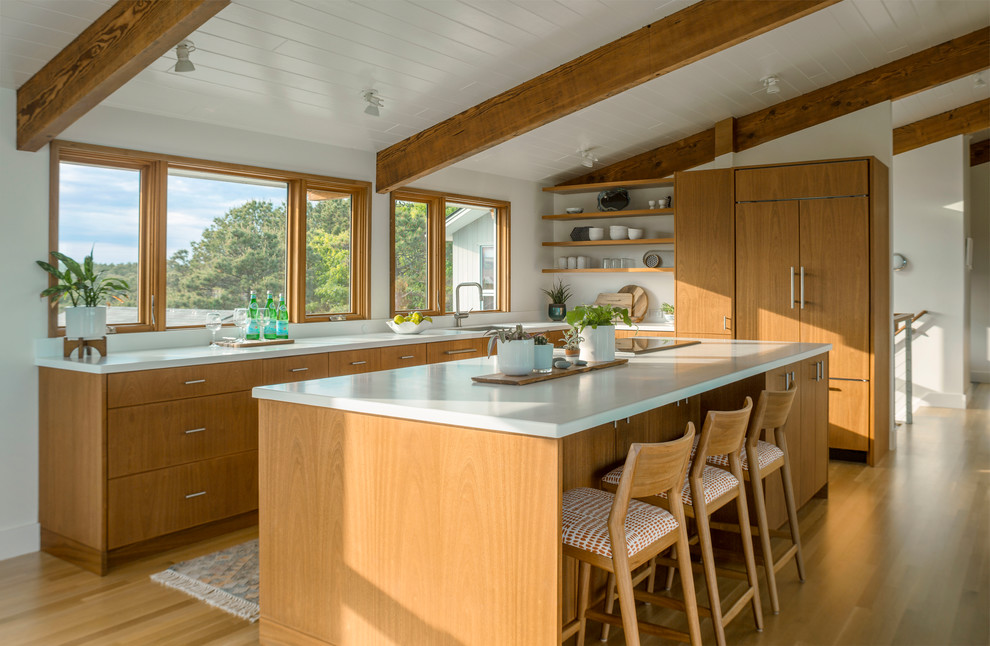Beach style l-shaped kitchen in Boston with an undermount sink, flat-panel cabinets, medium wood cabinets, window splashback, panelled appliances, medium hardwood floors, with island and white benchtop.