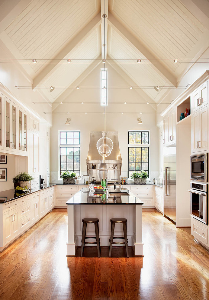 Inspiration for an expansive traditional u-shaped kitchen in Raleigh with shaker cabinets, white cabinets, stainless steel appliances, an undermount sink, granite benchtops, medium hardwood floors, with island and black benchtop.