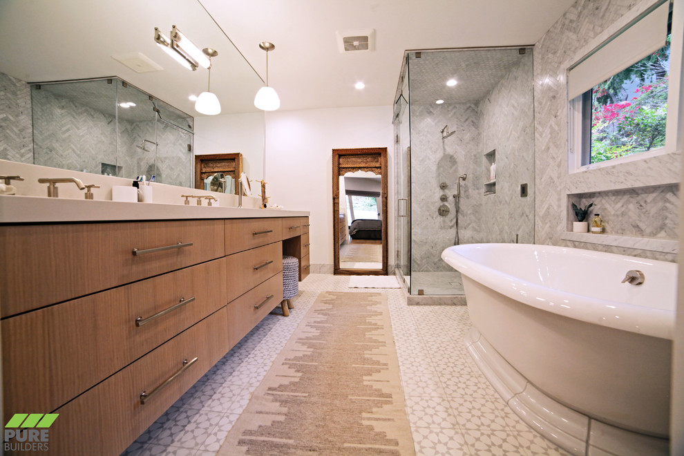 This is an example of a large contemporary master bathroom in Los Angeles with a freestanding tub, a corner shower, marble, white walls, ceramic floors, multi-coloured floor, a hinged shower door, flat-panel cabinets, medium wood cabinets, a bidet, an undermount sink, solid surface benchtops and beige benchtops.