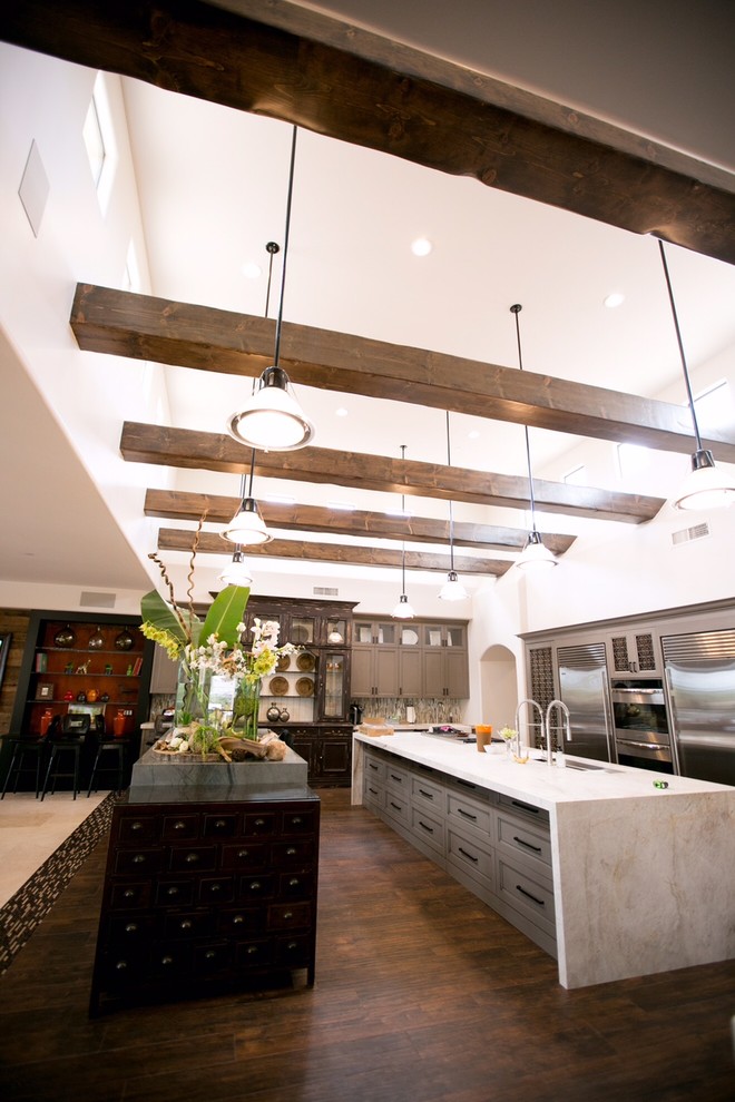 Design ideas for an expansive eclectic u-shaped open plan kitchen in Phoenix with a triple-bowl sink, recessed-panel cabinets, grey cabinets, quartzite benchtops, beige splashback, stone tile splashback, stainless steel appliances, dark hardwood floors and multiple islands.