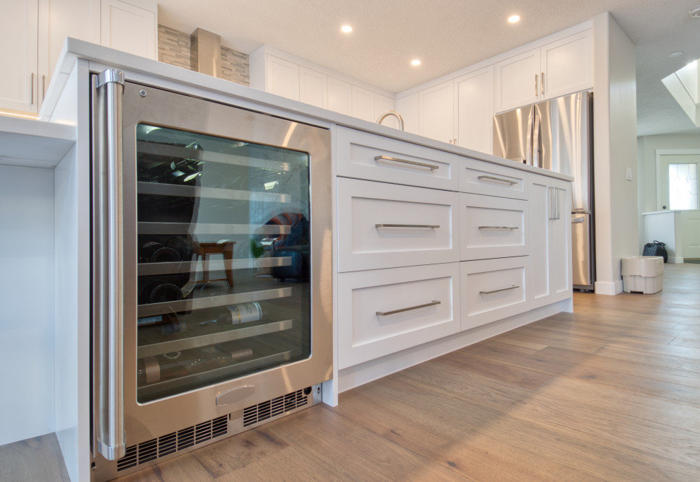 Inspiration for a large transitional u-shaped light wood floor and beige floor kitchen remodel in Calgary with an undermount sink, recessed-panel cabinets, white cabinets, quartz countertops, gray backsplash, matchstick tile backsplash, stainless steel appliances, an island and white countertops