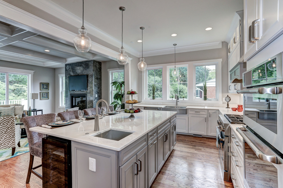 Photo of a large traditional u-shaped open plan kitchen in DC Metro with stainless steel appliances, with island, a farmhouse sink, recessed-panel cabinets, white cabinets, marble benchtops, white splashback, stone slab splashback and medium hardwood floors.
