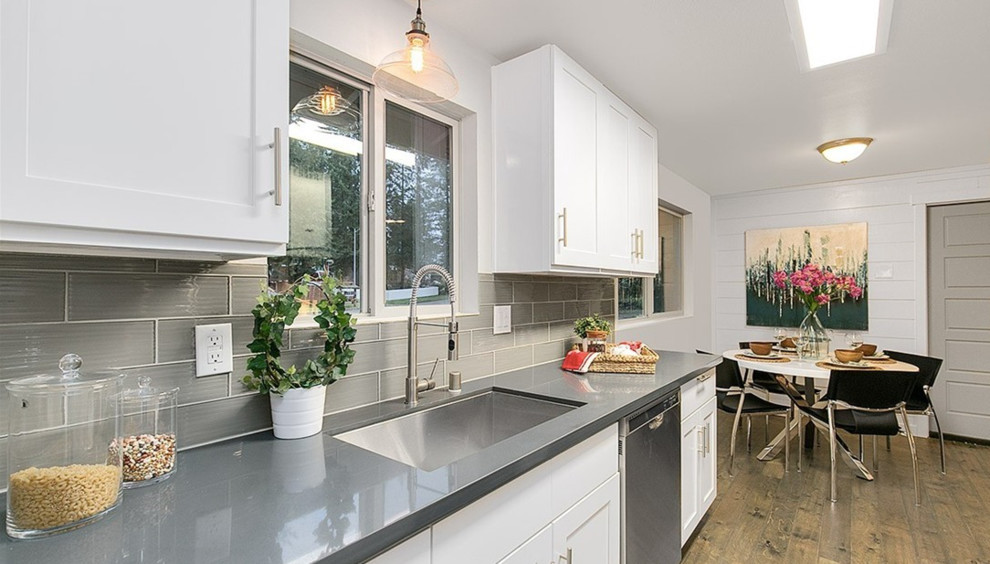 Small transitional galley dark wood floor open concept kitchen photo in Seattle with an undermount sink, recessed-panel cabinets, white cabinets, concrete countertops, gray backsplash, glass tile backsplash, stainless steel appliances and a peninsula