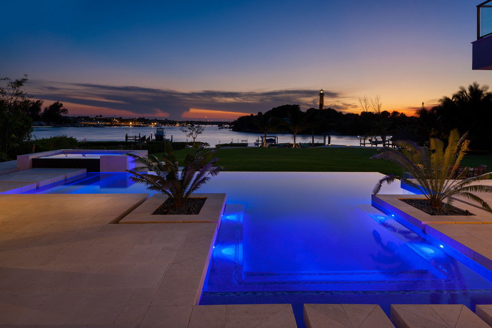 Inspiration for a large modern backyard custom-shaped infinity pool in Miami with natural stone pavers and a hot tub.