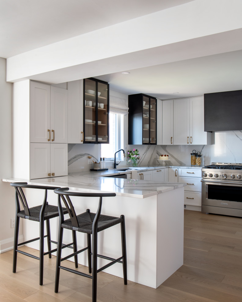 Inspiration for a mid-sized transitional u-shaped medium tone wood floor eat-in kitchen remodel with an undermount sink, shaker cabinets, white cabinets, quartz countertops, white backsplash, quartz backsplash, stainless steel appliances, a peninsula and white countertops