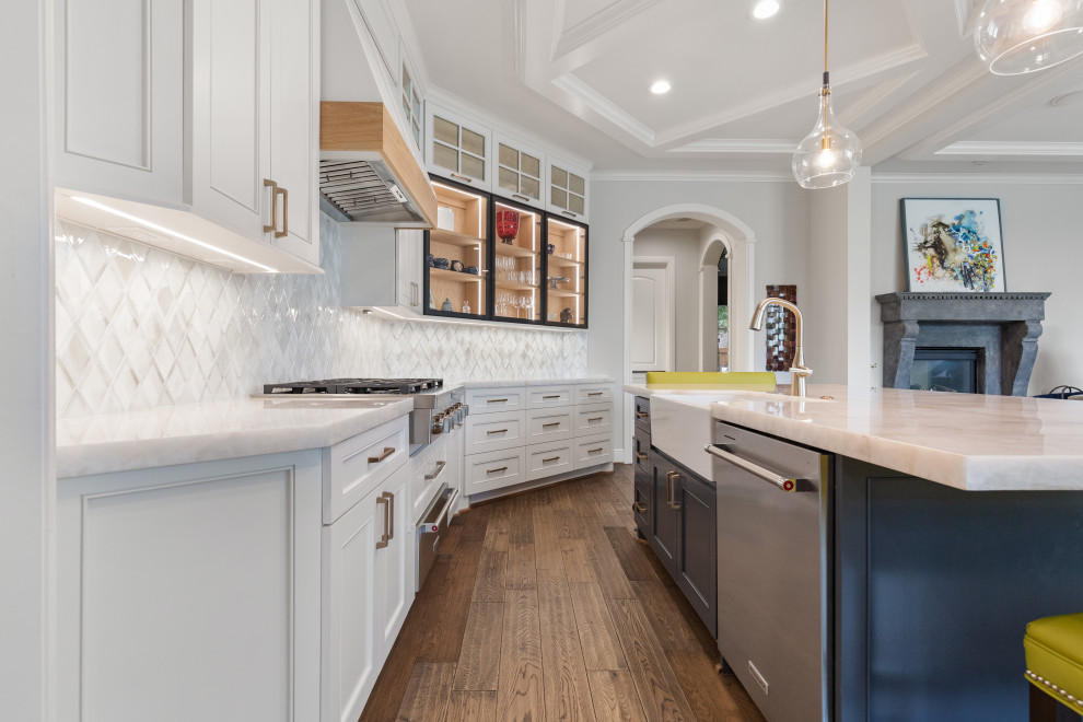Inspiration for a large transitional single-wall light wood floor and brown floor eat-in kitchen remodel in Houston with a farmhouse sink, recessed-panel cabinets, white cabinets, quartzite countertops, white backsplash, mosaic tile backsplash, stainless steel appliances, an island and white countertops