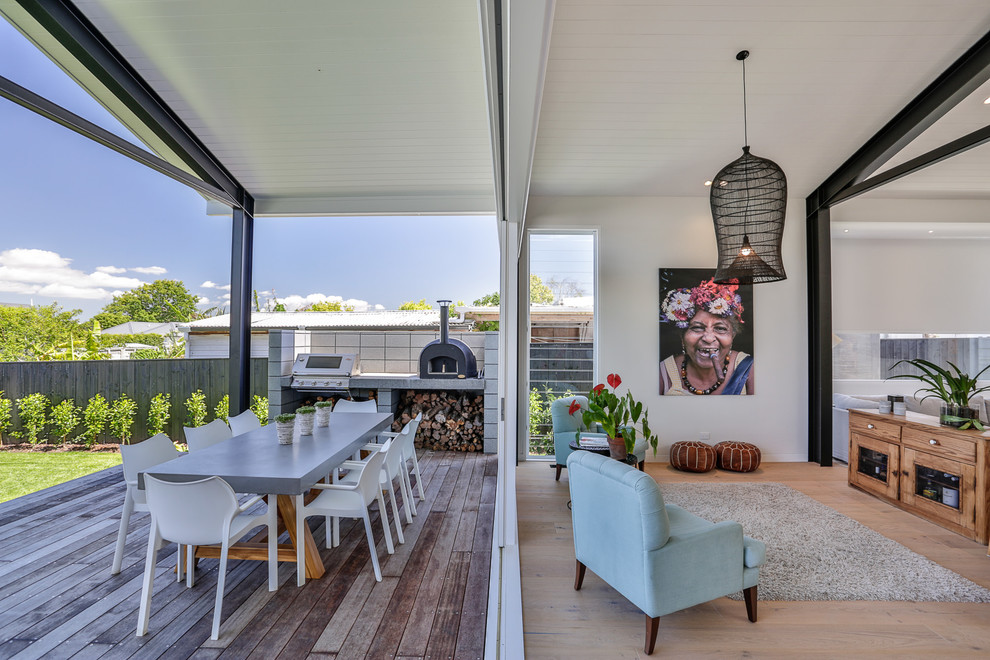 This is an example of a large transitional backyard deck in Auckland with a roof extension and an outdoor kitchen.