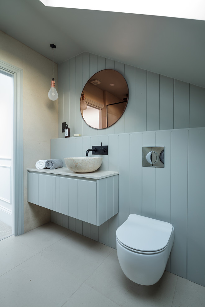 This is an example of a mid-sized scandinavian powder room in London with flat-panel cabinets, blue cabinets, a wall-mount toilet, blue walls, a vessel sink, grey floor and white benchtops.