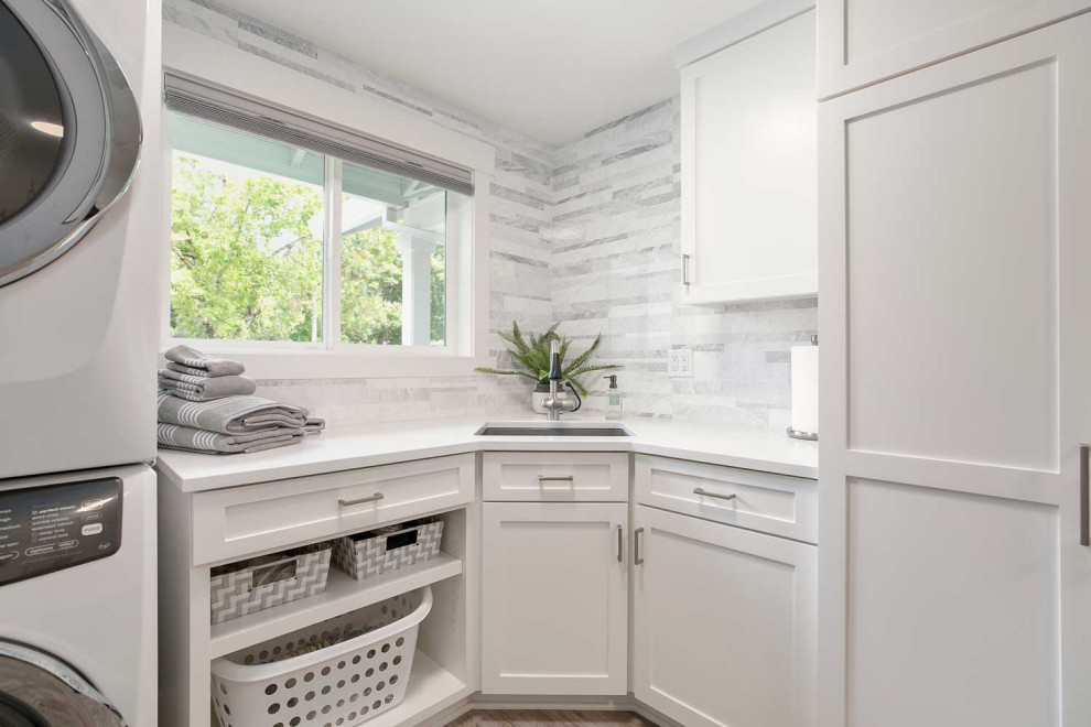 Mid-sized beach style l-shaped utility room in Portland with an undermount sink, shaker cabinets, white cabinets, quartz benchtops, grey splashback, vinyl floors, a stacked washer and dryer, grey floor and white benchtop.