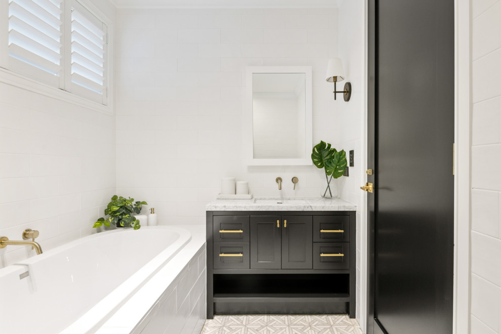 Photo of a country bathroom in Brisbane with shaker cabinets, black cabinets, a drop-in tub, white tile, white walls, an undermount sink, grey floor, grey benchtops, a single vanity and a built-in vanity.