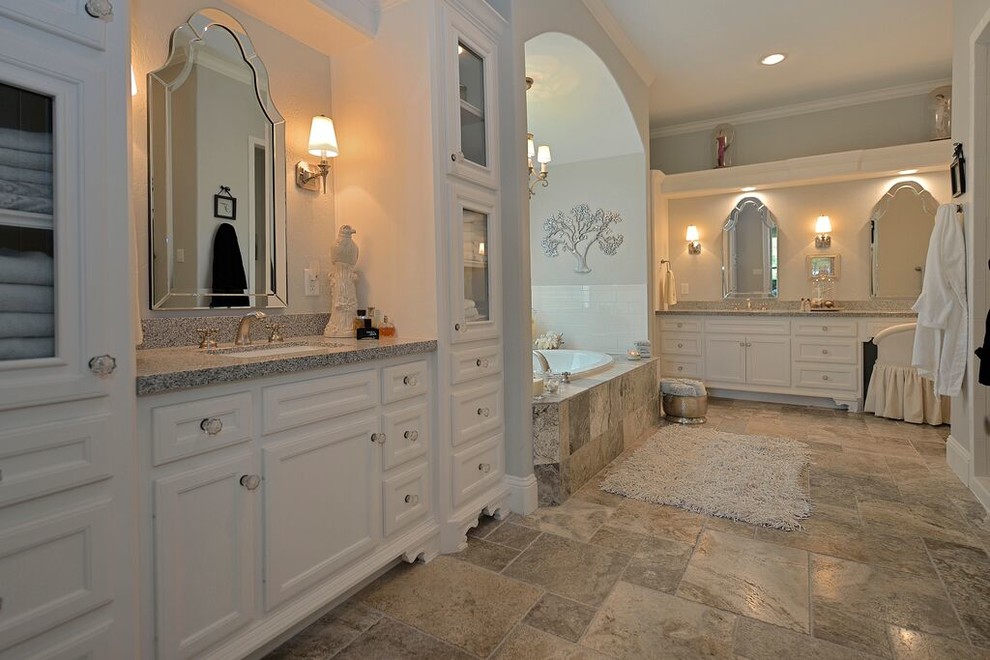 Photo of a large traditional master bathroom in Houston with an undermount sink, recessed-panel cabinets, white cabinets, engineered quartz benchtops, a drop-in tub, an open shower, a one-piece toilet, gray tile, stone slab, white walls and travertine floors.