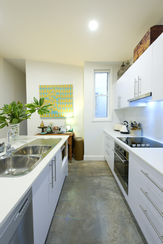 Small transitional single-wall open plan kitchen in Newcastle - Maitland with a double-bowl sink, flat-panel cabinets, white cabinets, solid surface benchtops, white splashback, glass sheet splashback, stainless steel appliances, concrete floors, with island and grey floor.