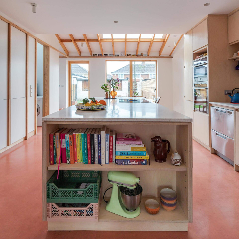 Cette image montre une grande cuisine ouverte parallèle design en bois clair avec un placard à porte plane, sol en béton ciré, îlot et un sol rose.