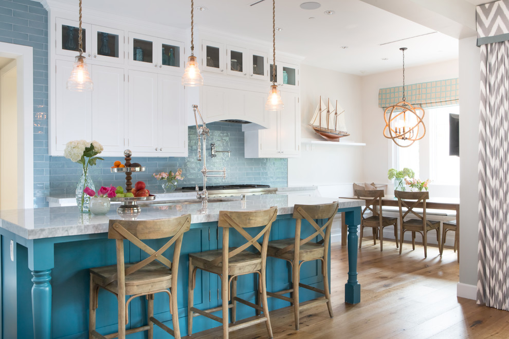 Photo of a beach style eat-in kitchen in Los Angeles with an undermount sink, shaker cabinets, white cabinets, blue splashback, subway tile splashback, stainless steel appliances, medium hardwood floors and with island.