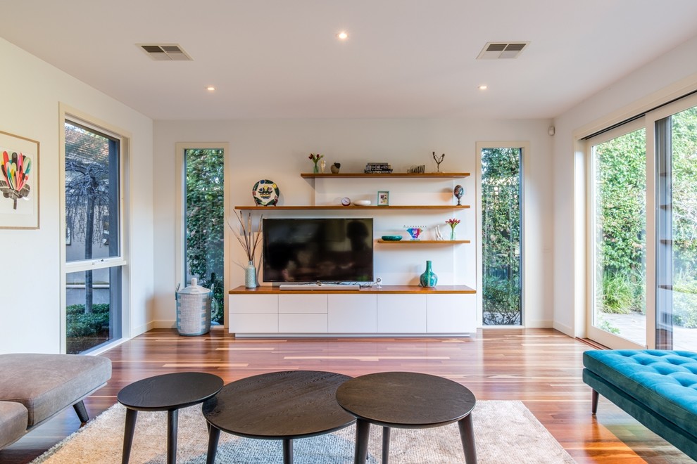 This is an example of a mid-sized contemporary living room in Melbourne with a freestanding tv, white walls, medium hardwood floors and no fireplace.