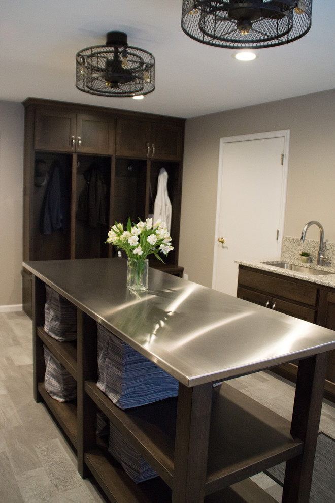Photo of a transitional utility room in Other with an utility sink, recessed-panel cabinets, granite benchtops, grey walls, a side-by-side washer and dryer and grey floor.