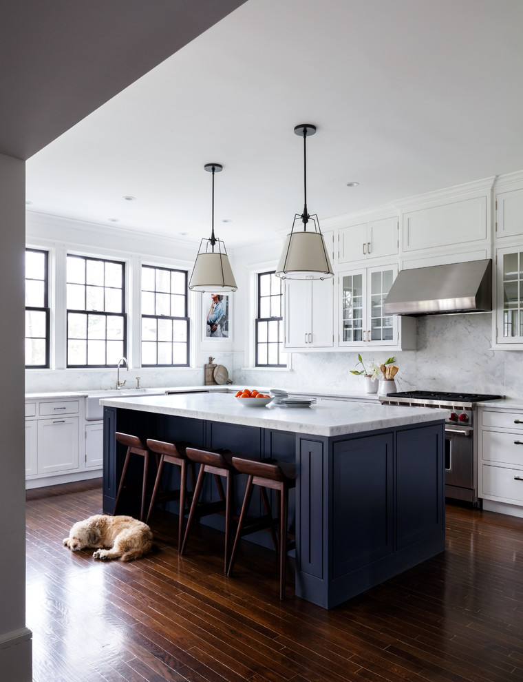 Design ideas for a transitional u-shaped separate kitchen in New York with a farmhouse sink, shaker cabinets, blue cabinets, grey splashback, marble splashback, stainless steel appliances, dark hardwood floors, with island, brown floor and grey benchtop.
