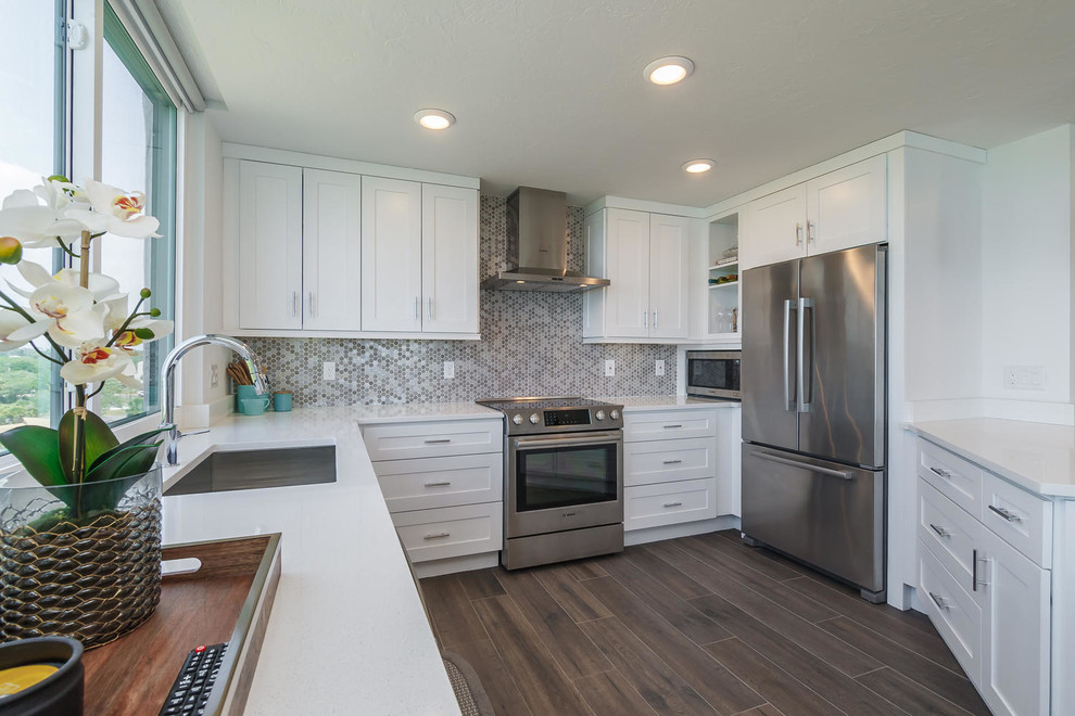 This is an example of a transitional u-shaped kitchen in Tampa with an undermount sink, shaker cabinets, white cabinets, metallic splashback, stainless steel appliances and dark hardwood floors.