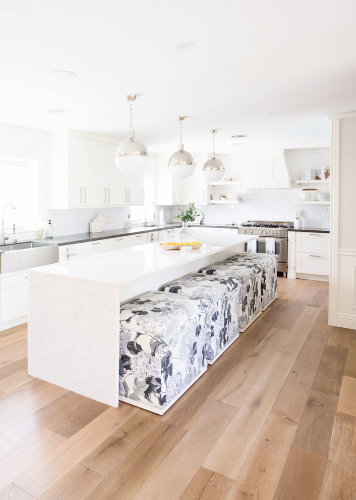 Large transitional u-shaped light wood floor and brown floor eat-in kitchen photo in Phoenix with a farmhouse sink, recessed-panel cabinets, white cabinets, quartz countertops, white backsplash, subway tile backsplash, stainless steel appliances, an island and white countertops