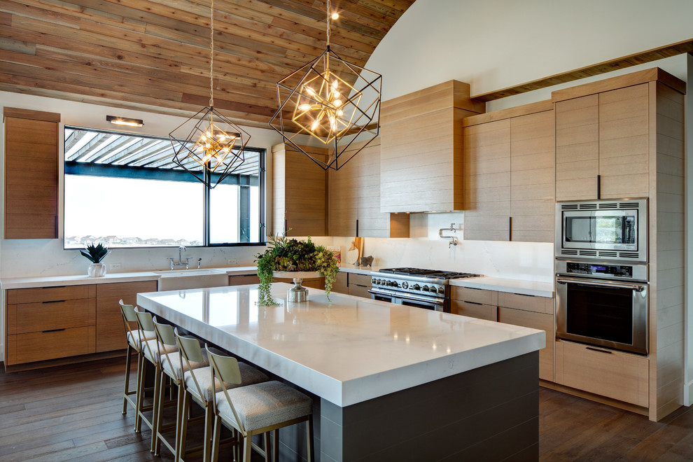 This is an example of a contemporary l-shaped eat-in kitchen in Other with a farmhouse sink, flat-panel cabinets, light wood cabinets, white splashback, stainless steel appliances, medium hardwood floors, with island, brown floor and white benchtop.