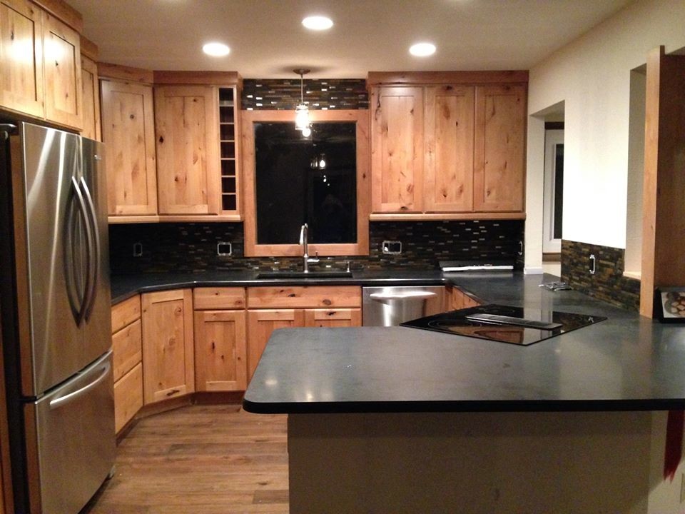 Example of a mid-sized mountain style u-shaped dark wood floor eat-in kitchen design in Denver with an undermount sink, flat-panel cabinets, light wood cabinets, granite countertops, green backsplash, glass tile backsplash, stainless steel appliances and a peninsula