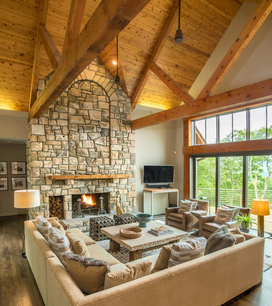 Large country open concept family room in Charlotte with beige walls, a standard fireplace, a stone fireplace surround, a wall-mounted tv, brown floor and medium hardwood floors.