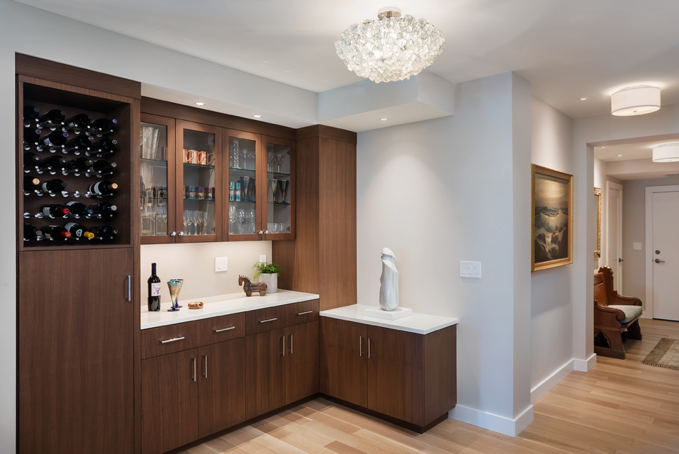 Inspiration for a mid-sized contemporary l-shaped home bar in Boston with flat-panel cabinets, dark wood cabinets, quartz benchtops, grey splashback, glass sheet splashback, light hardwood floors, beige floor and white benchtop.