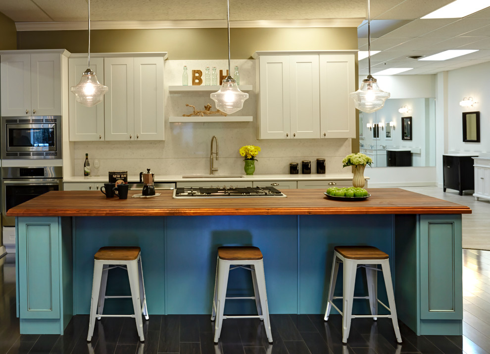 This is an example of a mid-sized beach style galley eat-in kitchen in Baltimore with an undermount sink, shaker cabinets, wood benchtops, white splashback, porcelain splashback, stainless steel appliances, with island, white cabinets, porcelain floors and brown floor.