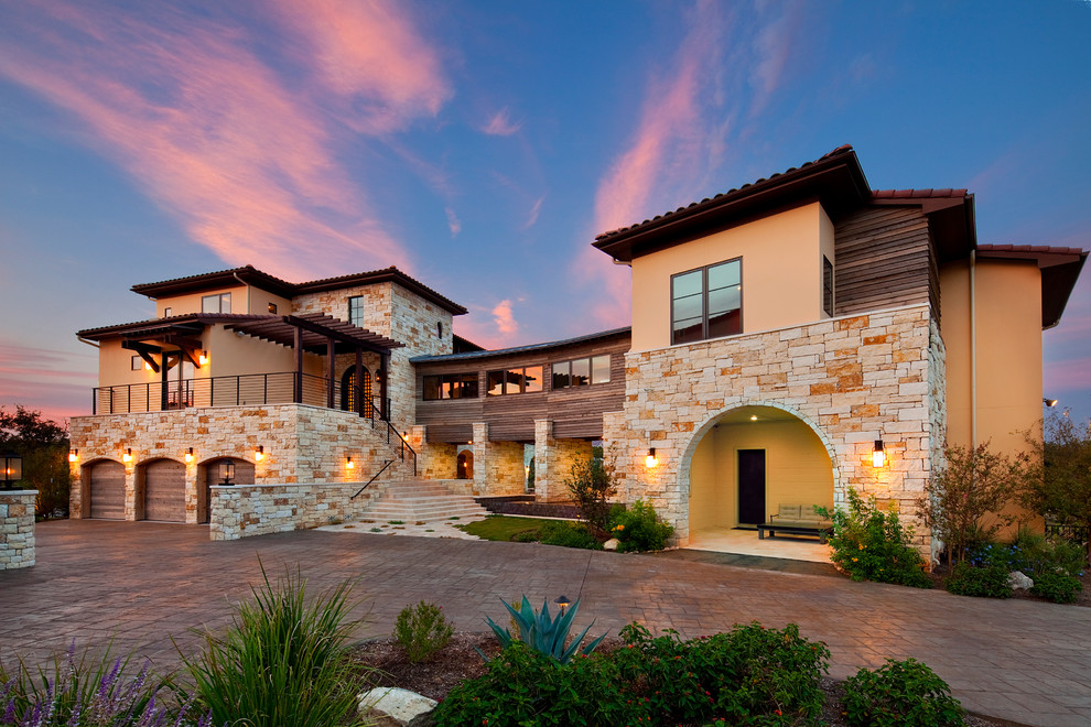 Photo of a large mediterranean three-storey beige house exterior in Austin with stone veneer, a flat roof and a shingle roof.