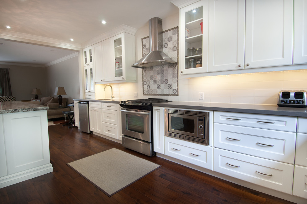 Inspiration for a large transitional u-shaped medium tone wood floor open concept kitchen remodel in Toronto with a double-bowl sink, shaker cabinets, white cabinets, quartzite countertops, white backsplash, ceramic backsplash, stainless steel appliances and an island