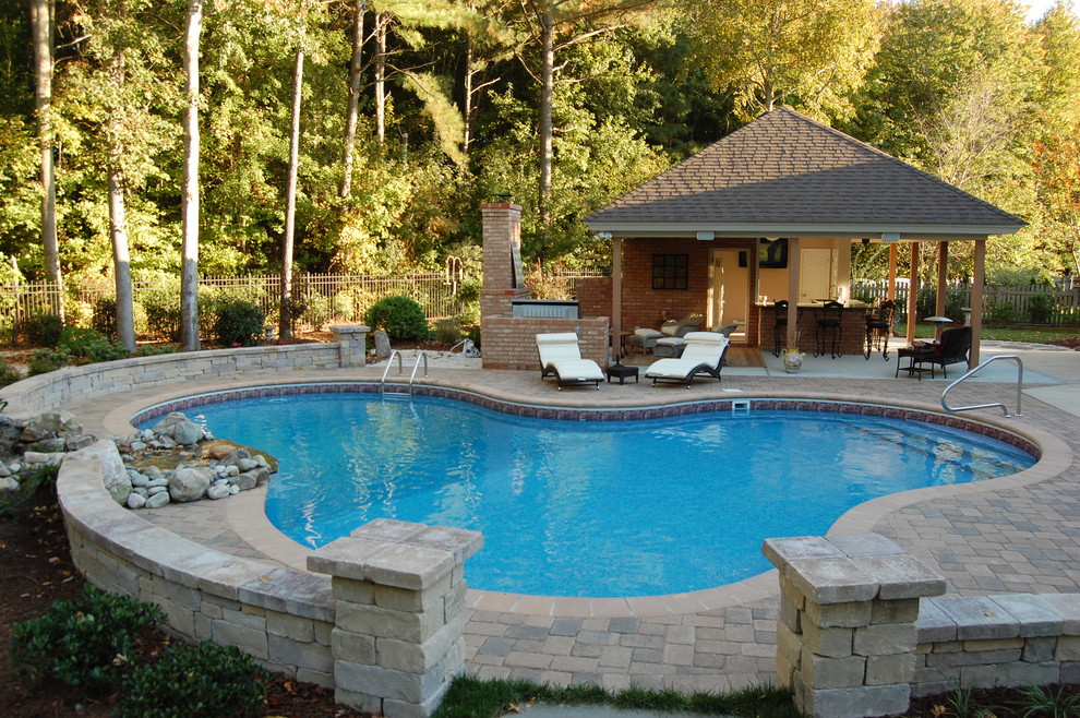 This is an example of a mid-sized arts and crafts backyard custom-shaped lap pool in Other with a pool house and concrete pavers.