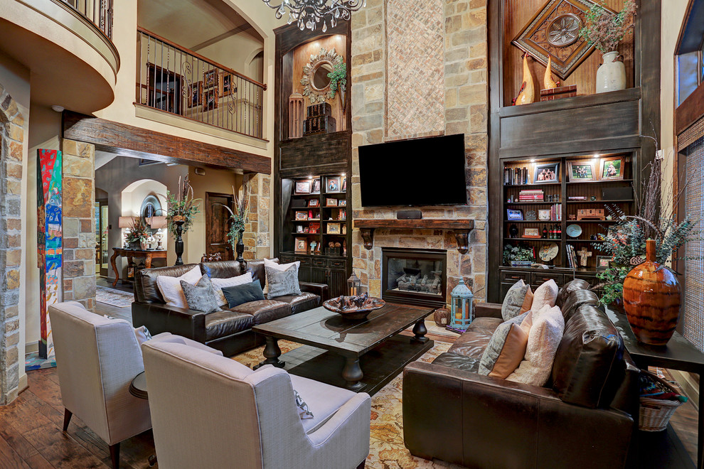 This is an example of a country open concept living room in Houston with beige walls, dark hardwood floors, a standard fireplace, a stone fireplace surround and a wall-mounted tv.