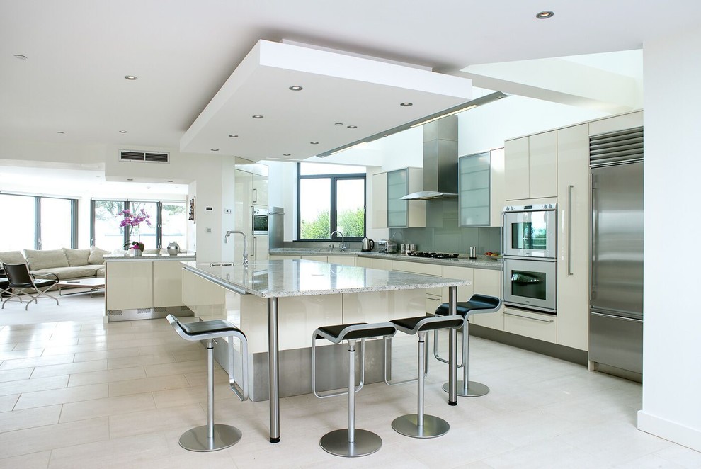 Inspiration for a contemporary open plan kitchen in Dorset with an undermount sink, flat-panel cabinets, beige cabinets, grey splashback, glass sheet splashback, stainless steel appliances, with island and beige floor.