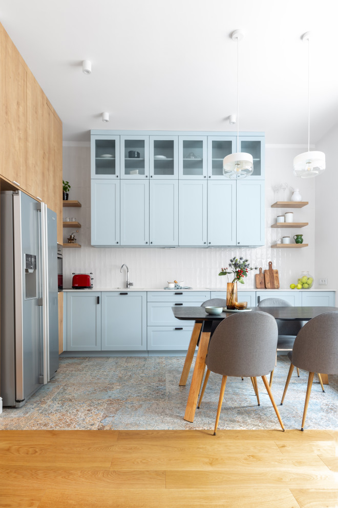 Design ideas for a mid-sized contemporary l-shaped open plan kitchen in Other with an undermount sink, glass-front cabinets, blue cabinets, quartz benchtops, white splashback, ceramic splashback, black appliances, porcelain floors, no island, multi-coloured floor and beige benchtop.